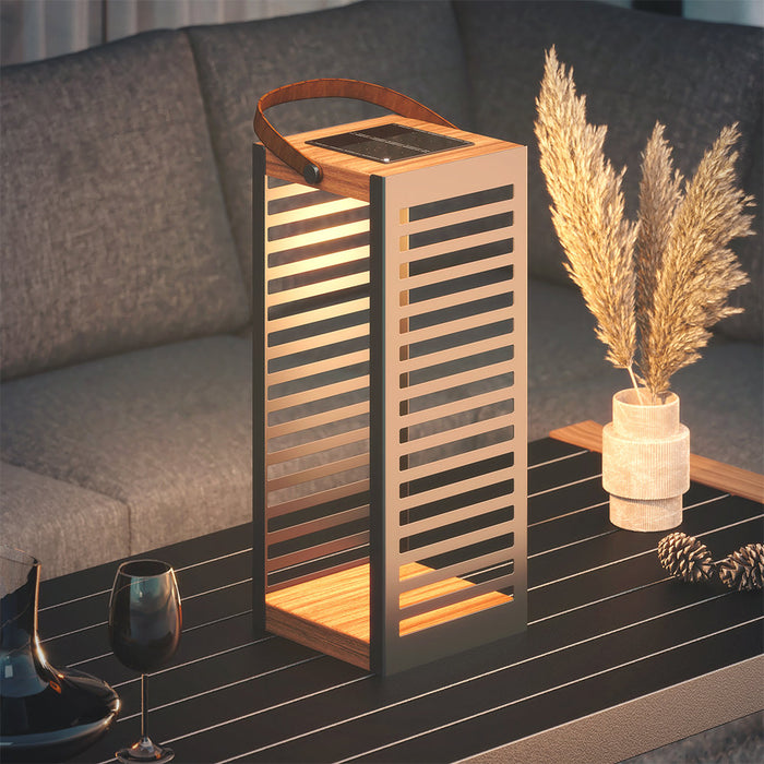 Wooden lantern with solar panel on a table next to a vase with dried plants.