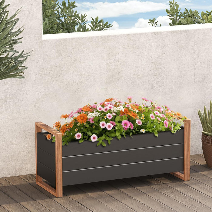 Gray planter box with wooden sides filled with colorful flowers on a wooden deck.