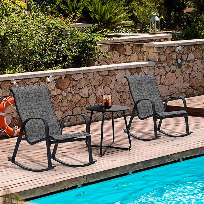 Two gray outdoor rocking chairs with a small table on a wooden deck by a pool.