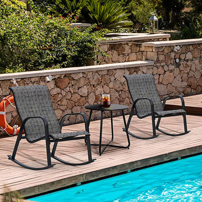 Two gray outdoor rocking chairs with a small table on a wooden deck by a pool.