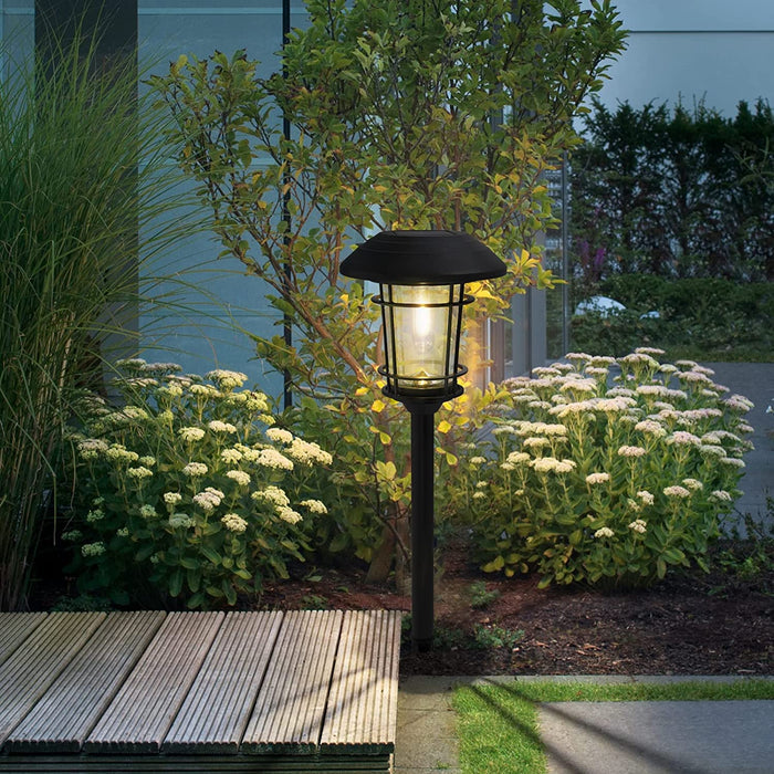Garden light fixture in a garden setting with flowers and a wooden bench.