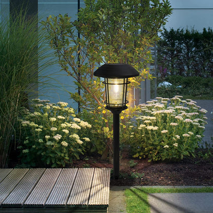 Garden light fixture in a garden setting with flowers and a wooden bench.