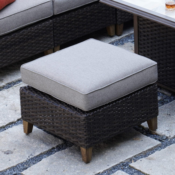 Wicker ottoman with a gray cushion on a stone patio